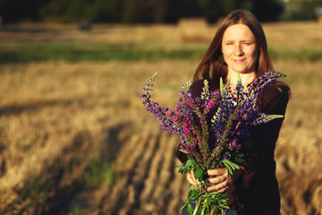 woman holding a bouquet of wildflowers lupines against rural landscape