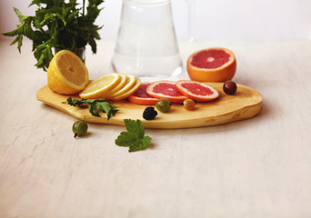 lemonade in pitcher, sliced lemon and grapefruit ,fresh berries and a bundle of fresh mint on a white background /a healthy lifestyle