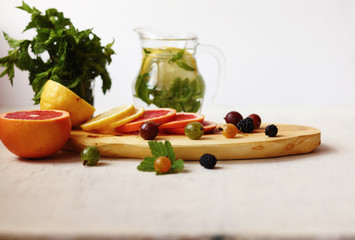 lemonade in pitcher, sliced lemon and grapefruit ,fresh berries and a bundle of fresh mint on a white background /a healthy lifestyle