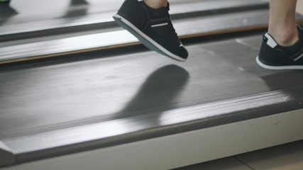 Closeup feet running back on treadmill in fitness gym.