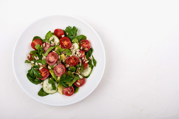 Salad with avocado, cucumbers, cherry tomatoes, spinach leaves, parsley and seeds on a white plate on a white background. Copy space.