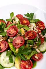 Salad with avocado, cucumbers, cherry tomatoes, spinach leaves, parsley and seeds on a white plate on a white background. Healthy vegetarian food.