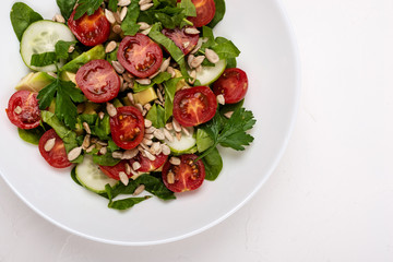 Salad with avocado, cucumbers, cherry tomatoes, spinach leaves, parsley and seeds on a white plate on a white background. Healthy vegetarian food.