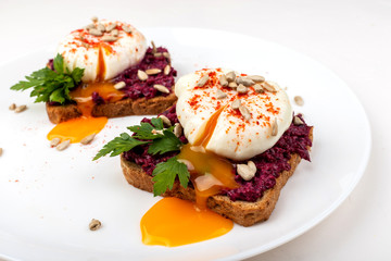 Poached eggs with homemade beetroot hummus, seeds and parsley on toast bread on a white plate on the white background. Healthy breakfast or snack