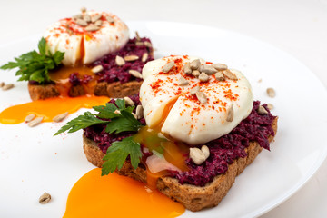 Poached eggs with homemade beetroot hummus, seeds and parsley on toast bread on a white plate on the white background. Healthy breakfast or snack