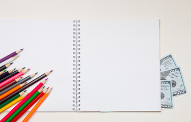 colored pencils lie on a white notebook with a spring and readable sheets of dollars banknotes money on a white table pencil sharpening sharpen color top view spring copybook copy space