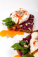 Poached eggs with homemade beetroot hummus, seeds and parsley on toast bread on a white plate on the white background. Healthy breakfast or snack
