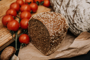 Fresh bread, cherry tomatoes on paper on wooden black background