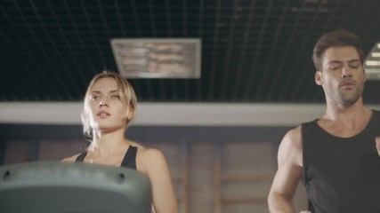 Concentrated couple running together on treadmill machine in gym club.