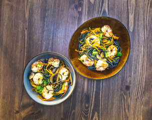 homemade black spaghetti with cuttlefish ink, with shrimp, dill and carrots. in a two bowl on a wooden table. healthy home dinner