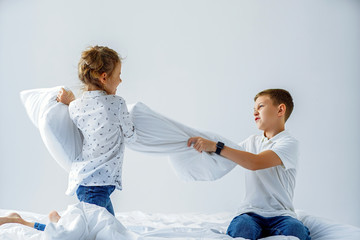 Naughty twins girl and boy friendly fighting staged a pillow fight on the bed in the bedroom. They like that kind of game.