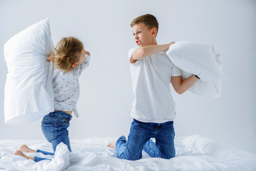 Naughty twins girl and boy friendly fighting staged a pillow fight on the bed in the bedroom. They like that kind of game.