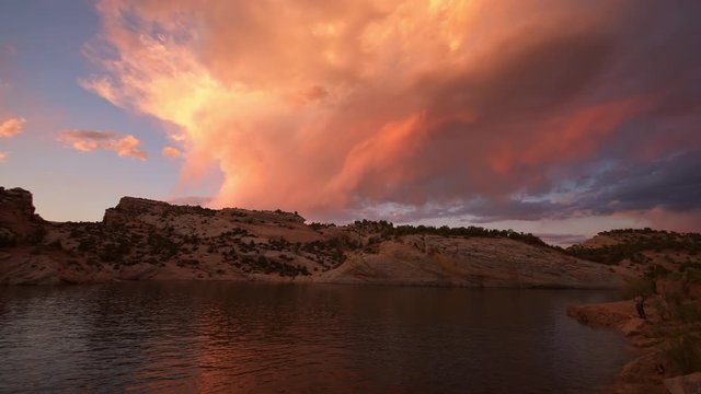 Tilting down from colorful sunset to shoreline of lake in slow motion in the Utah desert.