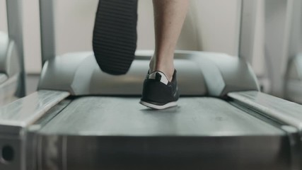 Closeup feet starting run on treadmill in fitness gym. Back view of black shoes