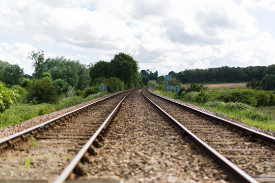 An empty train track, there are 2 tracks leading to a vanishing point on the horizon in rural countryside