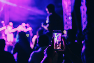 Person taking photo or recording video of live music concert with smartphone at night