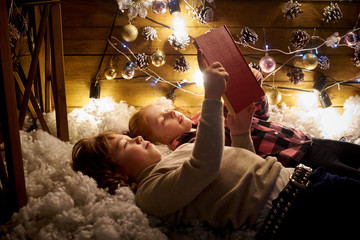 Fototapeta na wymiar Little girl and boy are reading a book in a decorated room for Christmas.