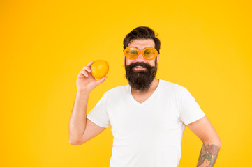 Cheerful guy hold ripe orange citrus fruit. Summer vacation. Refreshment source. Summer nutrition. Hipster with beard in summer mood. Man bearded hipster in orange sunglasses on yellow background