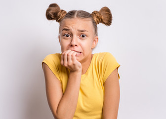 Portrait of surprised or shocked teen girl, on gray background. Funny child looking at camera with hand on mouth, biting nails. Beautiful caucasian teenager with opening wide eyes looking stressed.