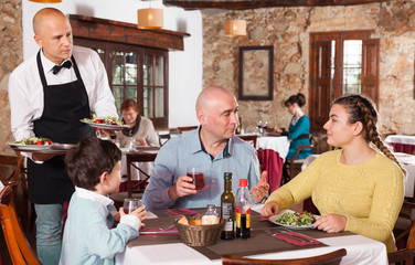 Waiter serving salad to family