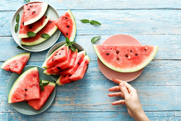 Fresh red watermelon slice, female hand on an blue rustic wood background with copy space.  Top view. Summertime concept.