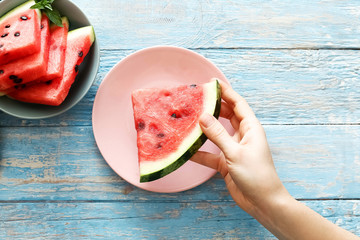   Top view fresh red watermelon slice in female hand on a pink plate on an blue rustic wood background.
