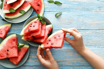 Top view fresh red watermelon slice in female hands on an blue rustic wood background. Sliced ripe...
