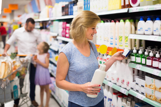 Woman selecting shampoo in supermarket.