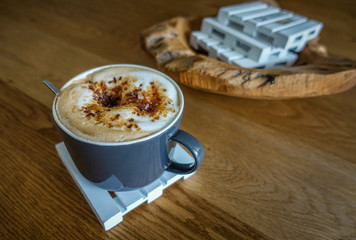 A nice cup of cappuccino on a coaster with a handful of candied sugar
