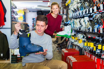 Saleswoman is helping man to trying on boots for skiing
