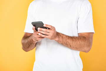 cropped view of man in white t-shirt using smartphone isolated on yellow