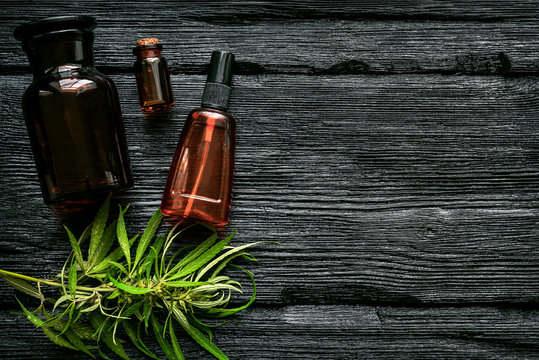 Cannabis cbd oil in bottle and green leaves on a black wooden table flat lay background.