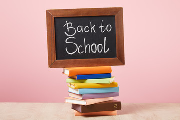 Chalkboard with back to school inscription on stack of books isolated on pink