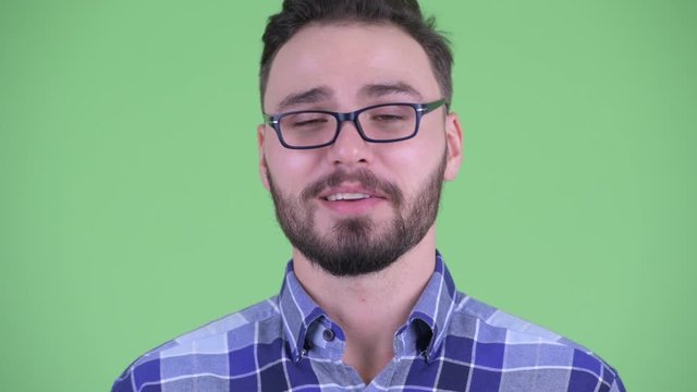 Face of happy young bearded hipster man talking