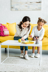 happy mother looking at daughter drawing while sitting on sofa