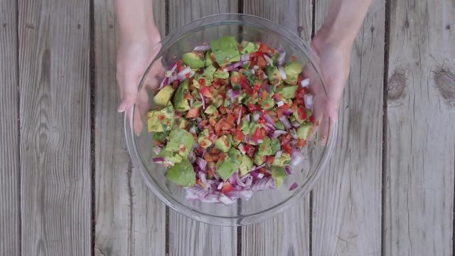Hands spin a bowl of guac ingredients around on a wooden background, diet 4k.