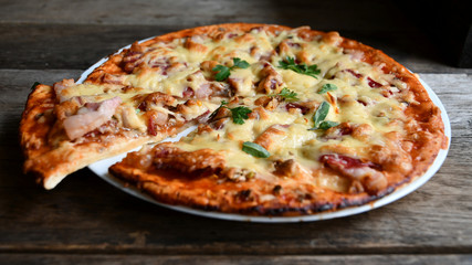 Homemade pizza with cheese, tomatoes, bacon and herbs in a white ceramic plate on a wooden table.