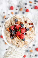 Healthy oatmeal served with berries, chocolate chips, almonds and honey over a marble table background. Shot from top view.
