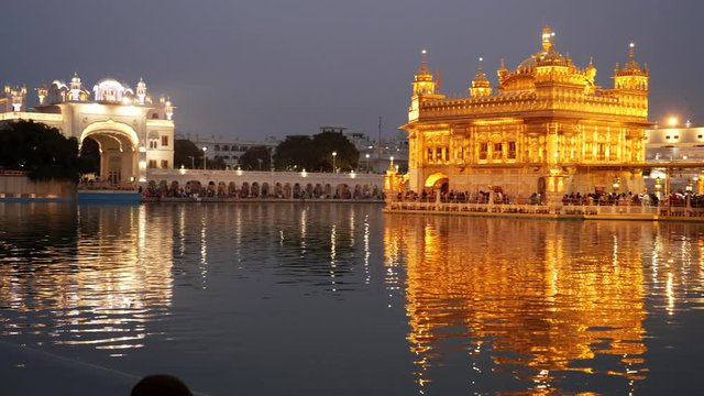 panning shot of the golden temple complex and sacred pool at night in amritsar, india