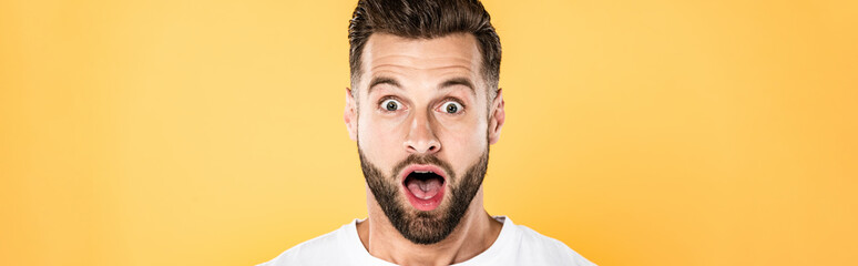 panoramic shot of shocked handsome man in white t-shirt with open mouth isolated on yellow