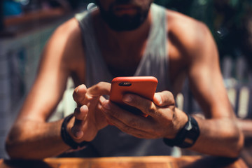 young guy with a beard in a shirt and headphones,Young and smiling man sitting on the roof with mobile phone and listening music (intentional sun glare and vintage color, focus on mobile phone