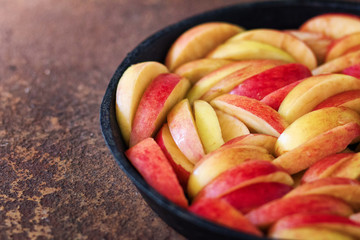 The apple cut by pieces in a black pig-iron frying pan on a rusty metal surface. Preparation for apple pie. Front view. 