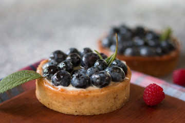Tartlets with blueberries on the wooden board with a checkered napkin, with fresh berries of raspberry. Top view