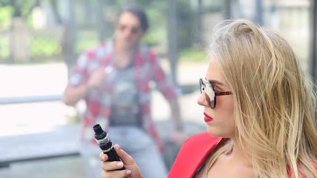 Stylish couple in a city. Two people use the electronic cigarette
