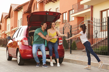 Cute girl running to her parents near family car on street