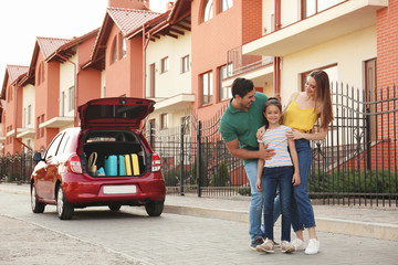 Happy parents hugging their daughter near family car on street