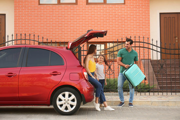 Happy family with suitcase near their car on street