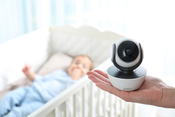 Woman holding baby camera near crib with child in room. Video nanny