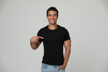 Handsome young African-American man in blank t-shirt on light background. Space for design