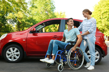 Young woman with disabled man in wheelchair near car outdoors